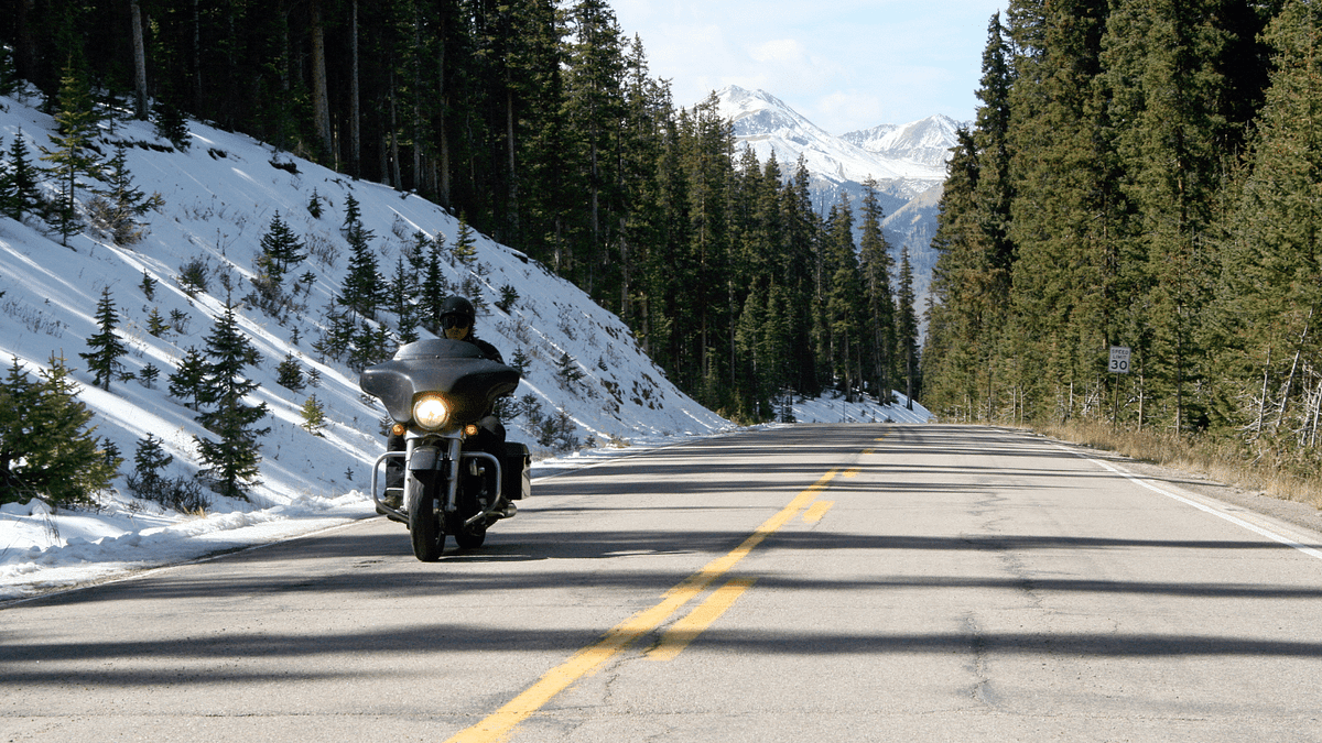 Someone riding a motorcycle next to snowy mountains.